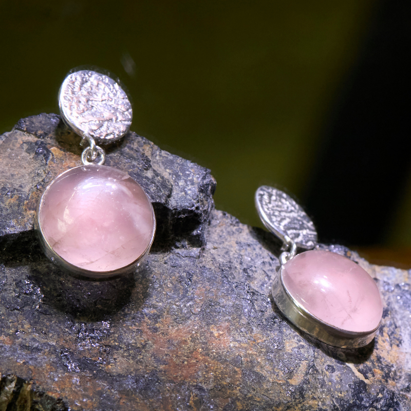 handcrafted rose quartz silver earrings displayed on natural rock