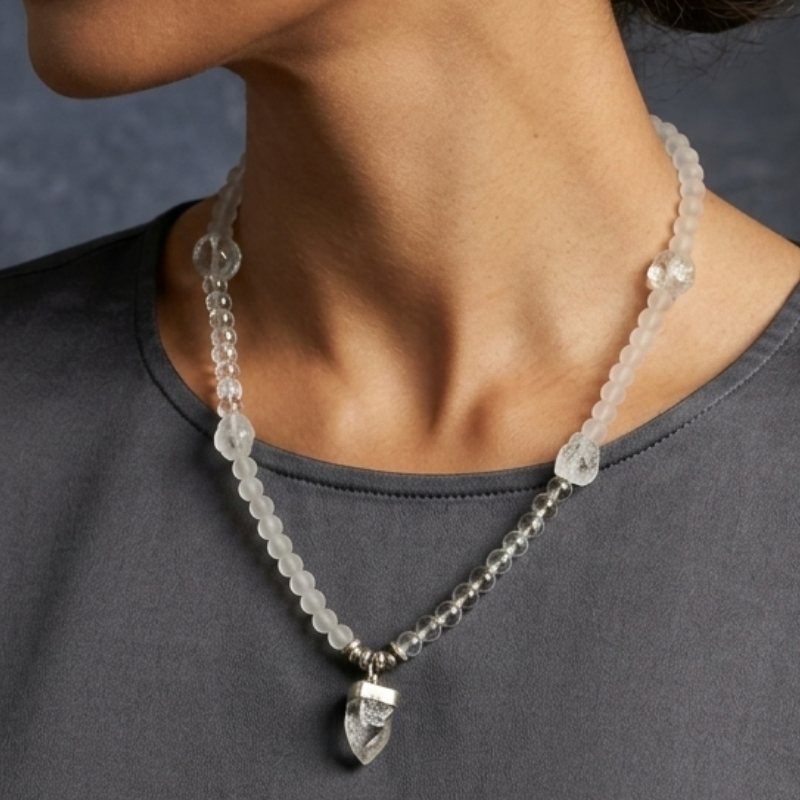 A high-jewelry boutique portrait of a model with her hair in a bun, wearing the Crystal Arrowhead Mala necklace, which rests elegantly on a charcoal silk top, showcasing its versatile length.