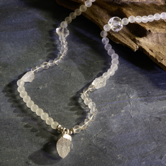 Premium natural crystal mala necklace on a textured dark slate background, featuring a mix of frosted "moon-glow" beads, raw crystal points, and a central hand-carved quartz arrowhead pendant.