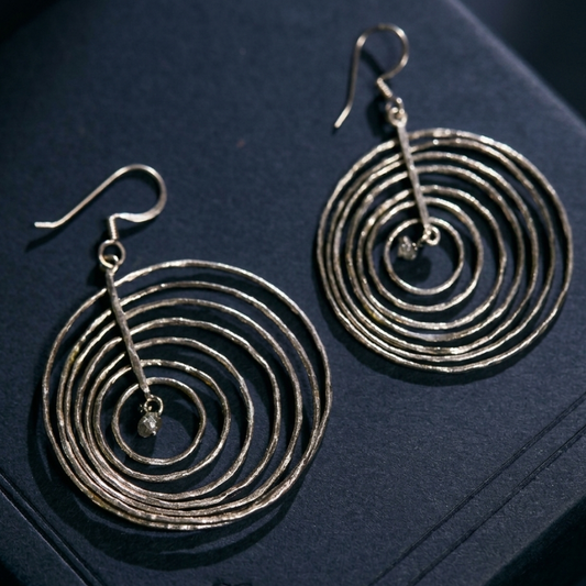 Pair of Celestial Orbit earrings handcrafted in 925 sterling silver featuring hammered concentric circles and raw crystal drops on a dark background.